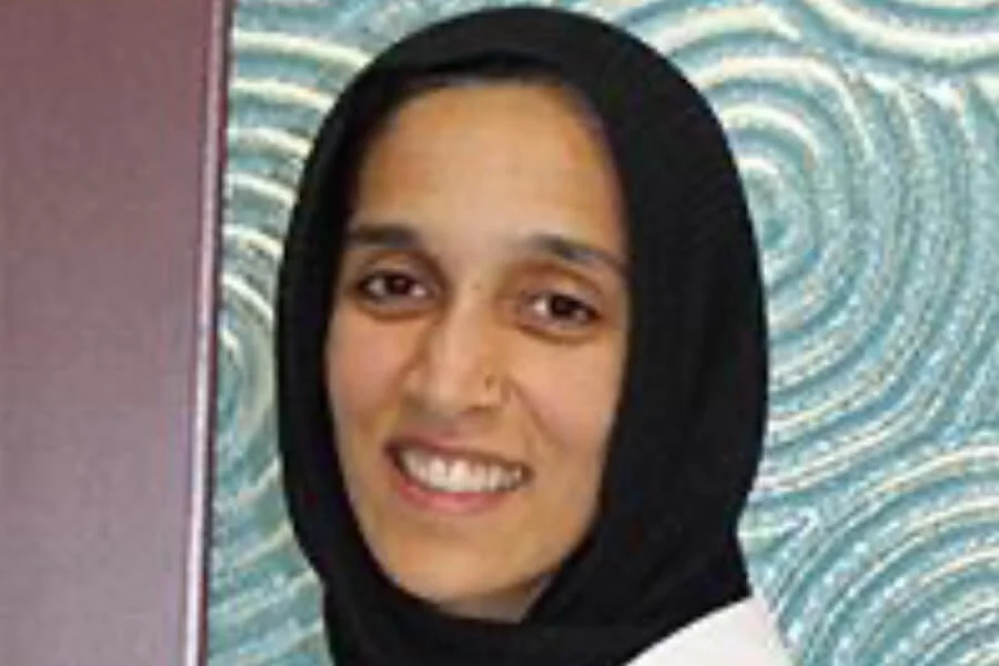 Professional photo of Dr. Aisha Chaudhry wearing a black hijab and smiling warmly in front of a textured blue background, representing trusted and compassionate care – IC Laser Eye